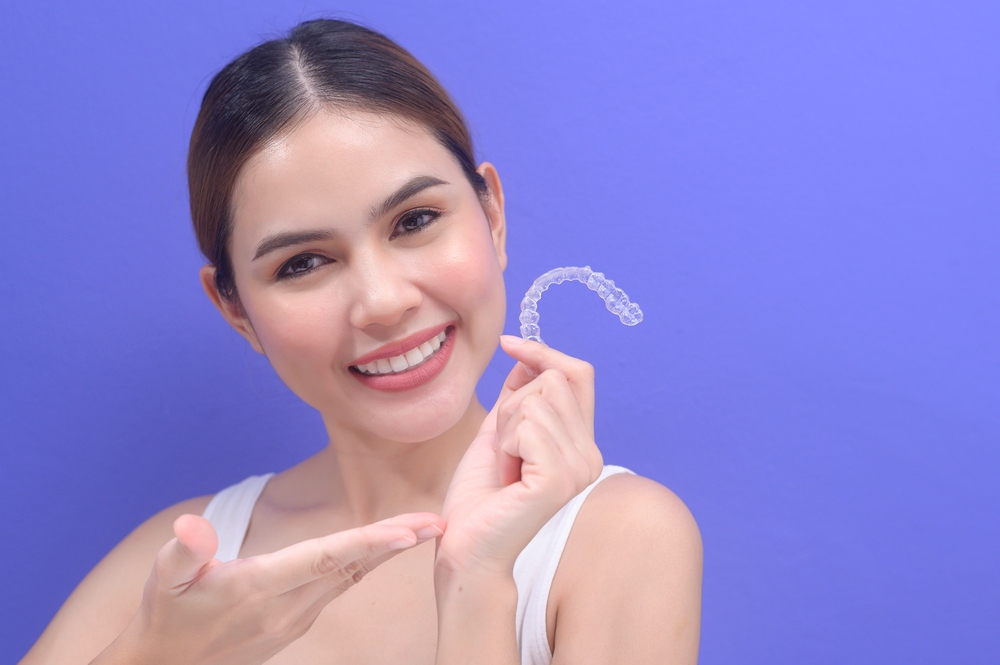 young smiling woman holding invisalign clear aligners - Can Invisalign Fix Overbite in Indianapolis, IN