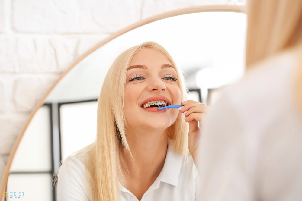 young woman metal braces toothbrush home - How to Floss with Braces in Indianapolis, IN